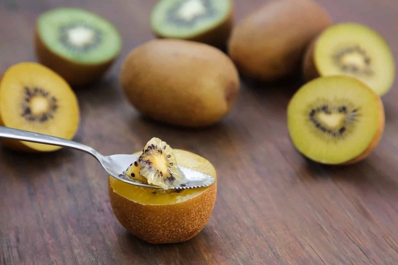 Image of sliced kiwi fruits with one half topped with yogurt on a wooden table, showcasing delicious and nutritious snack options.