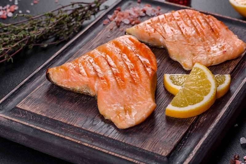 Fresh cooked salmon with lemon wedges on wooden board, healthy dog treat.