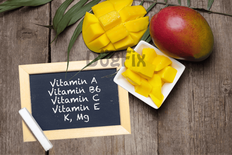 Healthy mango fruit with chopped cubes, whole mango, and chalkboard displaying vitamins for dogs.