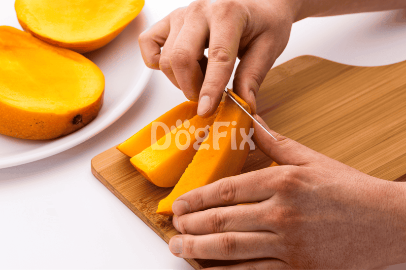 Image of hands slicing ripe mango on a wooden board with mango pieces in the background.