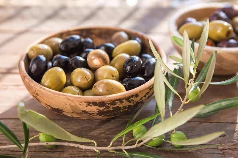 Organic black and green olives in wooden bowls on rustic table.