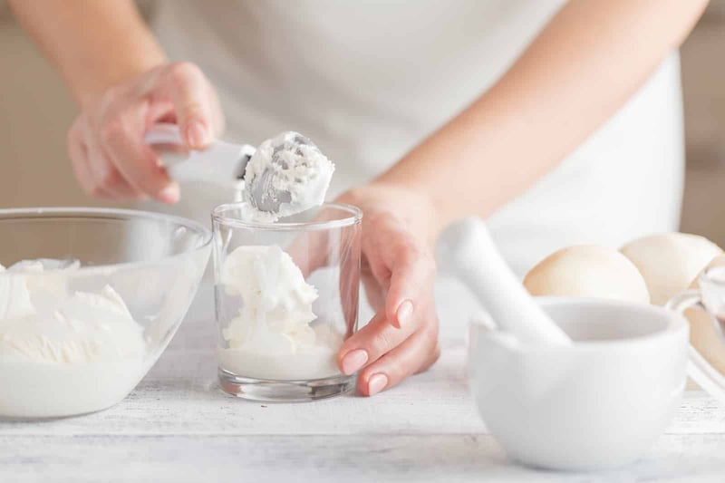 Alt text: Person scooping homemade ice cream into a glass, with bowls of ingredients on the table.