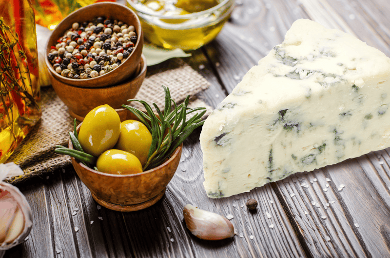 Delicious blue cheese accompanied by herbs, spices, and olive oil on a wooden table.