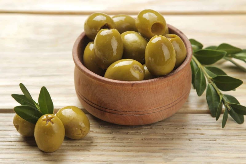 Bright green olives in a wooden bowl with fresh leaves, perfect for dog treats and healthy snacks.