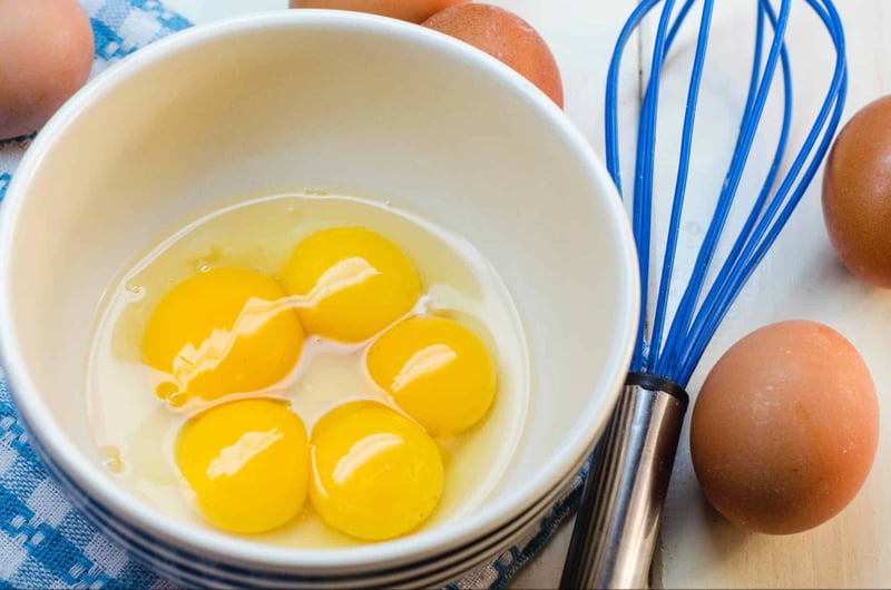 Bright yellow eggs in a white bowl on a kitchen counter.
