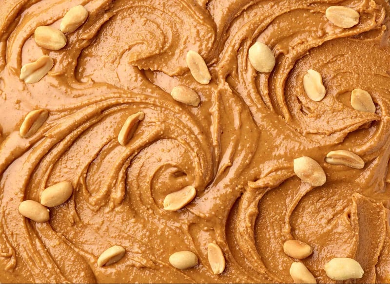 Close-up of caramel peanut spread, creamy and smooth with scattered peanuts.