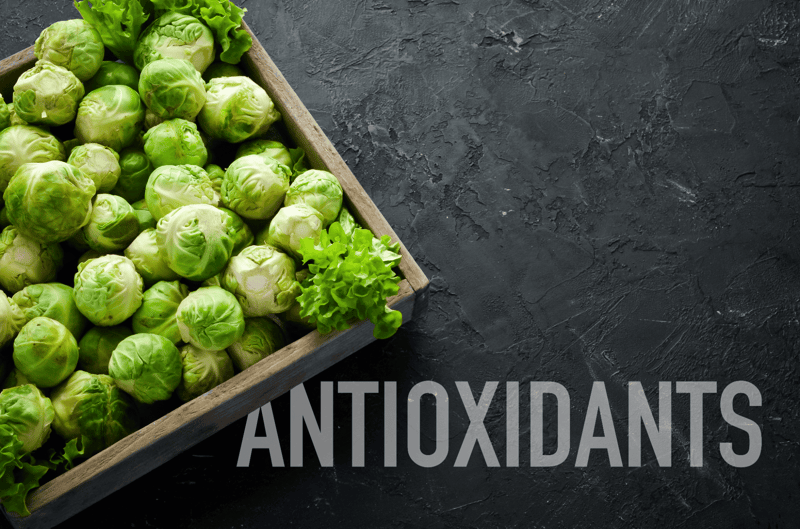 Fresh green Brussels sprouts with a leafy garnish on black textured background.