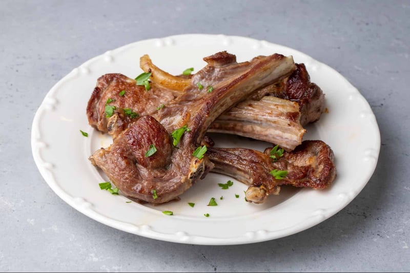 Delicious cooked lamb chops garnished with fresh herbs on a white plate. Perfect for dog-friendly, nutritious pet meals.