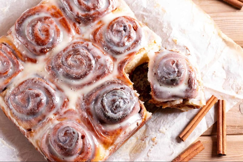 Delicious cinnamon roll cake with cream cheese glaze on parchment paper. Perfect for breakfast or dessert.