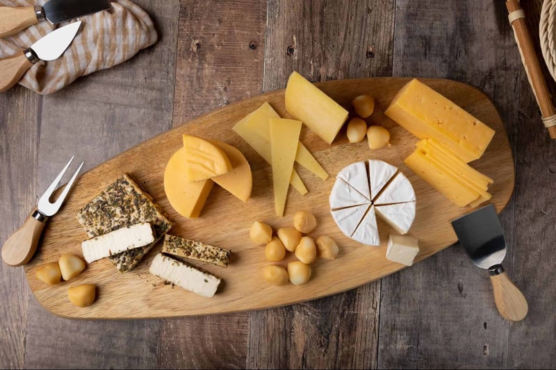 Varying cheese types including hard, soft, and blue cheese with nuts, served on a rustic wooden table.