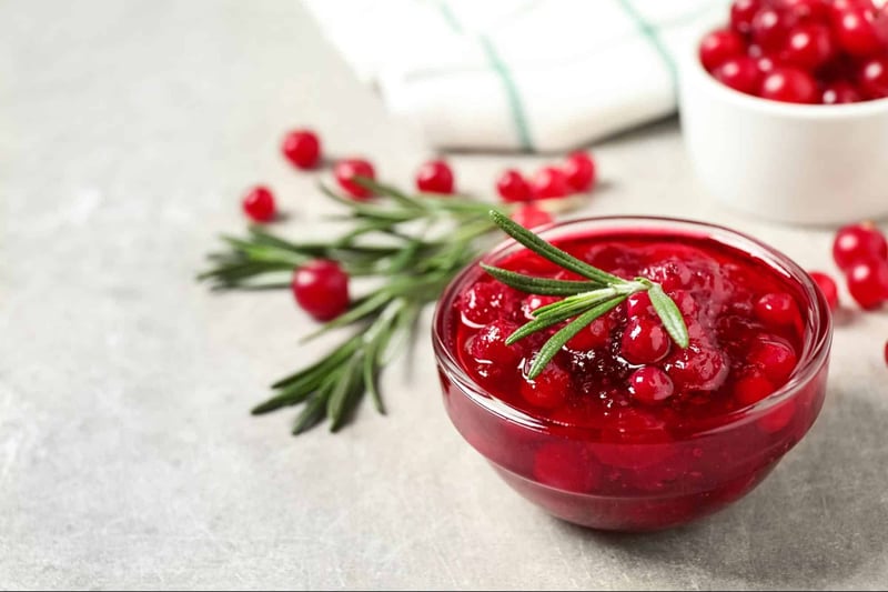Vibrant bowl of cranberry sauce garnished with rosemary, complemented by herb sprigs and a bowl of fresh cranberries.