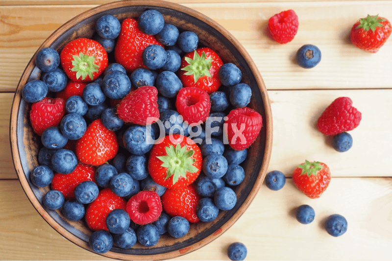 Bright strawberries, blueberries, and raspberries in a wooden bowl on a light wood surface.