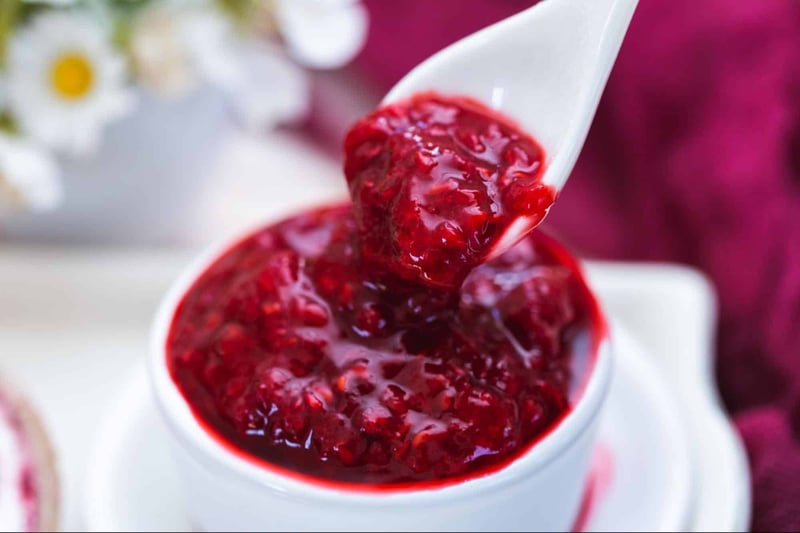 Close-up of vibrant red berry jam in a white spoon, ready for spreading or topping.