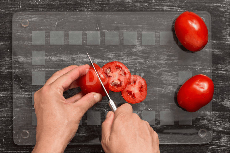 Close-up of hands slicing ripe tomatoes on a glass cutting board for nutritious dog snacks.