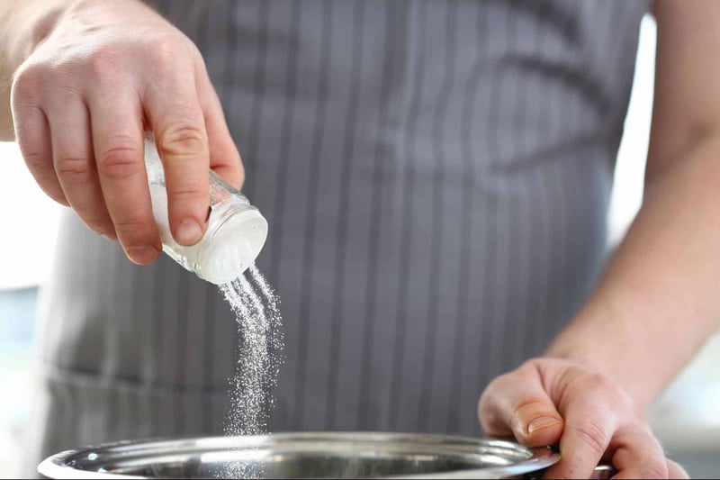 Person seasoning food with salt from a salt shaker.