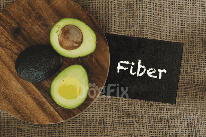 Avocado halves with seed on a wooden board, next to a chalkboard labeled "Fiber", highlighting healthy fats and dietary fiber.