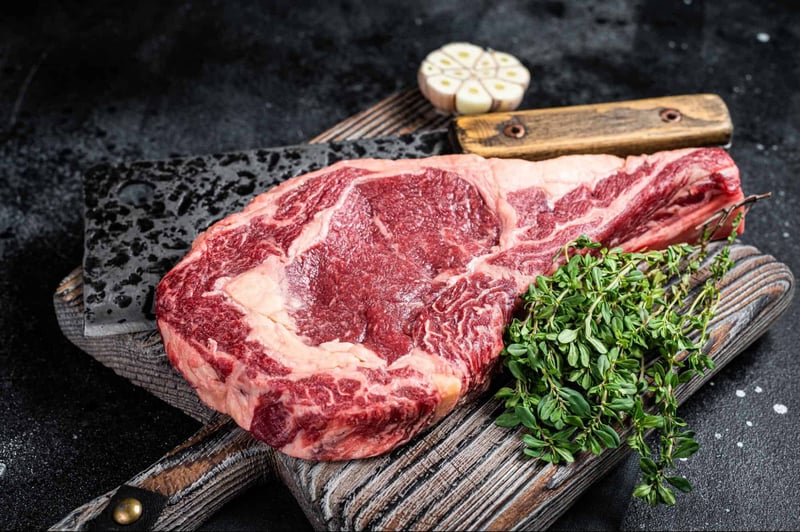 High-quality marbled beef steak on rustic cutting board with fresh herbs and garlic. Perfect for grilling or fine dining.