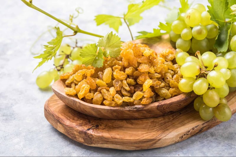Fresh green grapes and raisins on a wooden tray, safe dog treats high in antioxidants and vitamins.