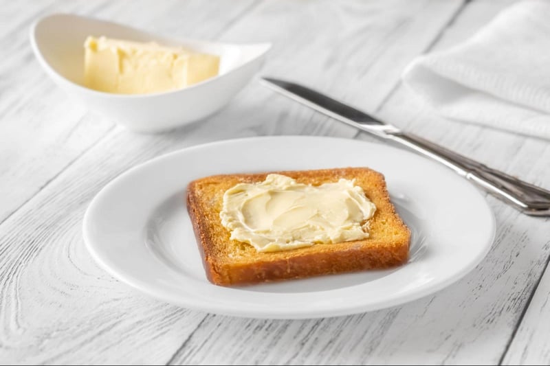 Delicious toasted bread with a generous spread of butter, served on a white plate with butter and a butter knife.