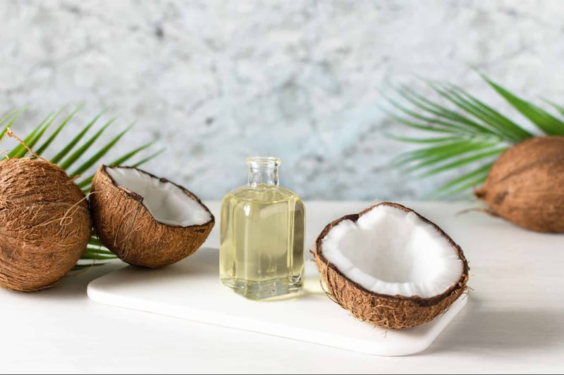 Natural coconut oil in a glass bottle with coconut halves on a white background.