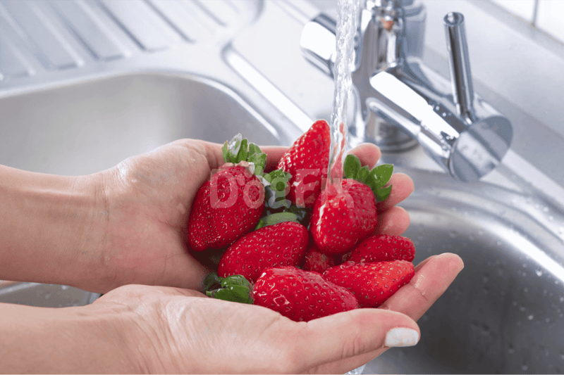 Delicious strawberries being rinsed under running water in a modern kitchen sink for healthy pet treats.