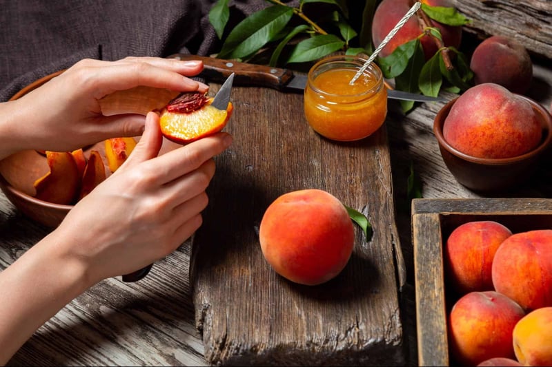 Close-up of hands preparing peach jam with fresh peaches and jam jar on rustic wooden table, healthy homemade fruit preserves.