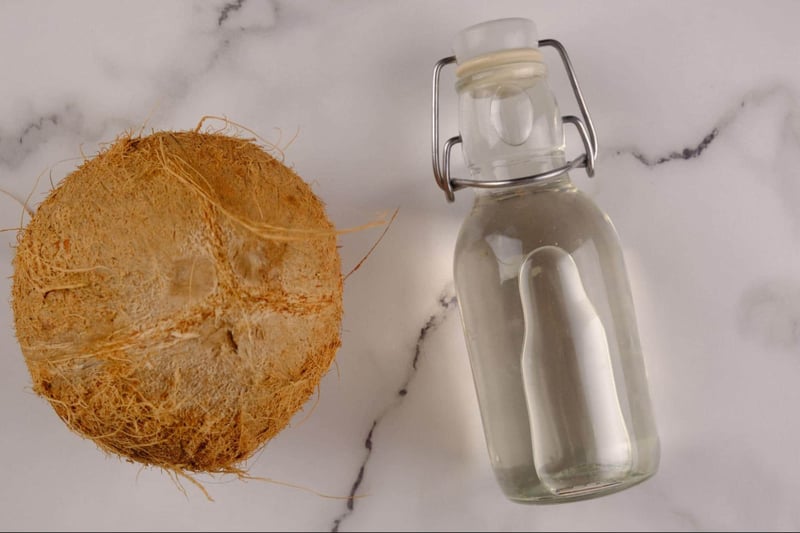 Natural coconut oil in a glass bottle with coconut halves on a white background.