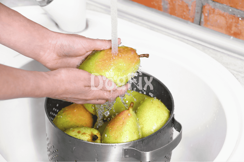 Hand washing fresh pears in a kitchen sink, preparing healthy dog treats with natural ingredients.
