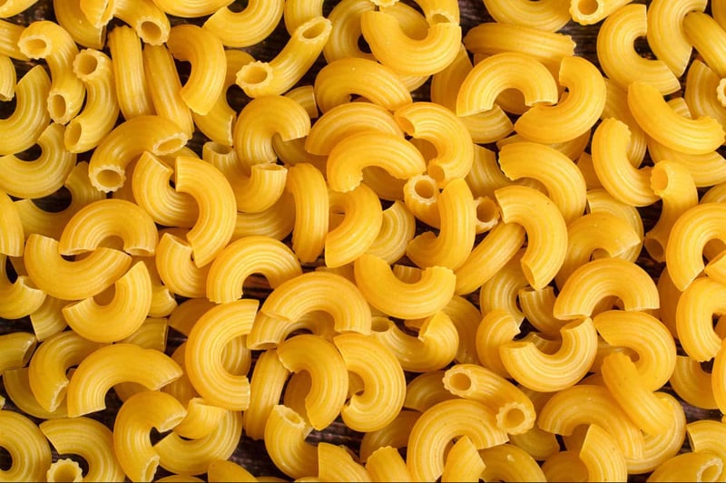 Vibrant yellow macaroni pasta scattered on a dark surface.