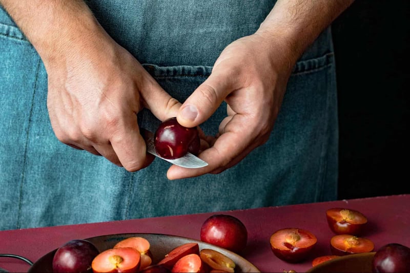Close-up of person slicing cherries with a knife, emphasizing fresh fruit preparation for a healthy lifestyle.