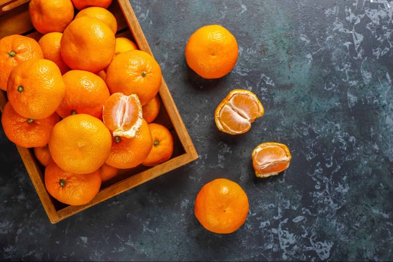 Vivid orange tangerines, some peeled, scattered on textured dark surface, highlighting fresh citrus fruits.