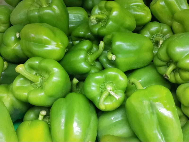 Bright green bell peppers with shiny skin, abundant at a fresh produce market.
