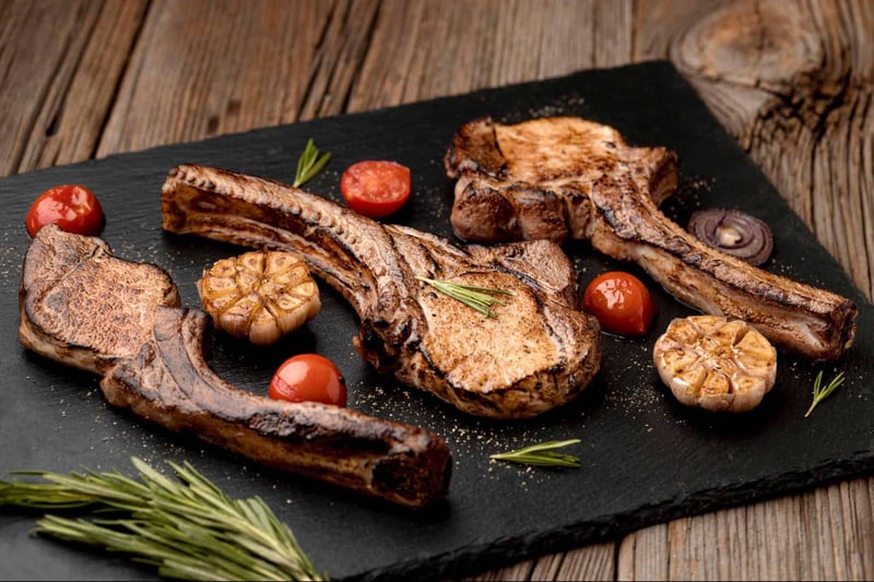 Close-up of grilled beef steaks with garlic, tomatoes, and herbs on a rustic wooden table.