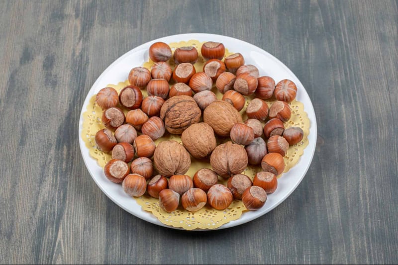 Fresh hazelnuts and walnuts arranged on a white plate for healthy dog treats.