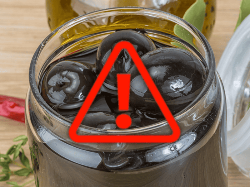 Bright red warning icon over jar of black olives with a warning symbol.