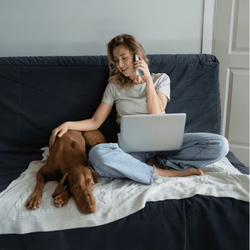 Woman and dog lounging together on sofa, enjoying a relaxed moment with technology.