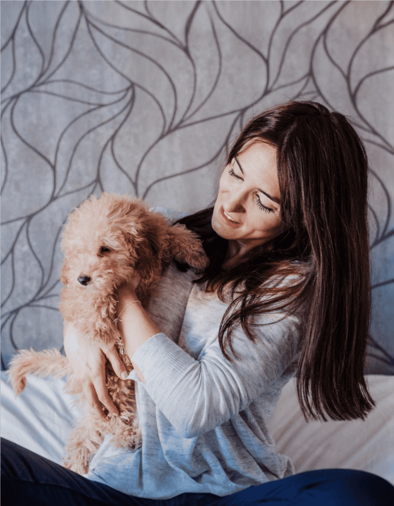 Friendly woman cuddling adorable small poodle puppy at home.