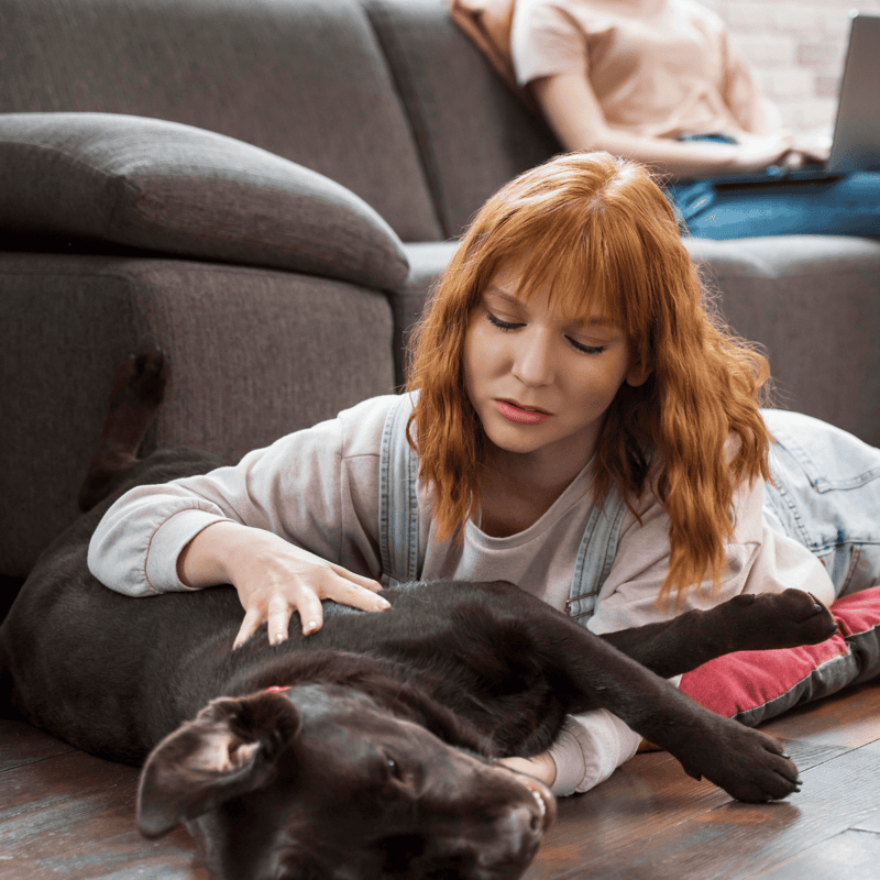 Female with red hair cuddling a black dog on the floor.