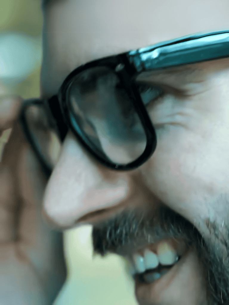 Close-up of a man with glasses smiling outdoors.