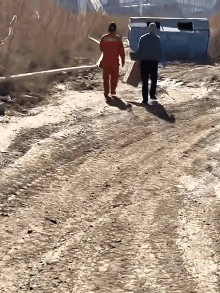 Rescue workers walking on rough dirt terrain near overturned vehicle.