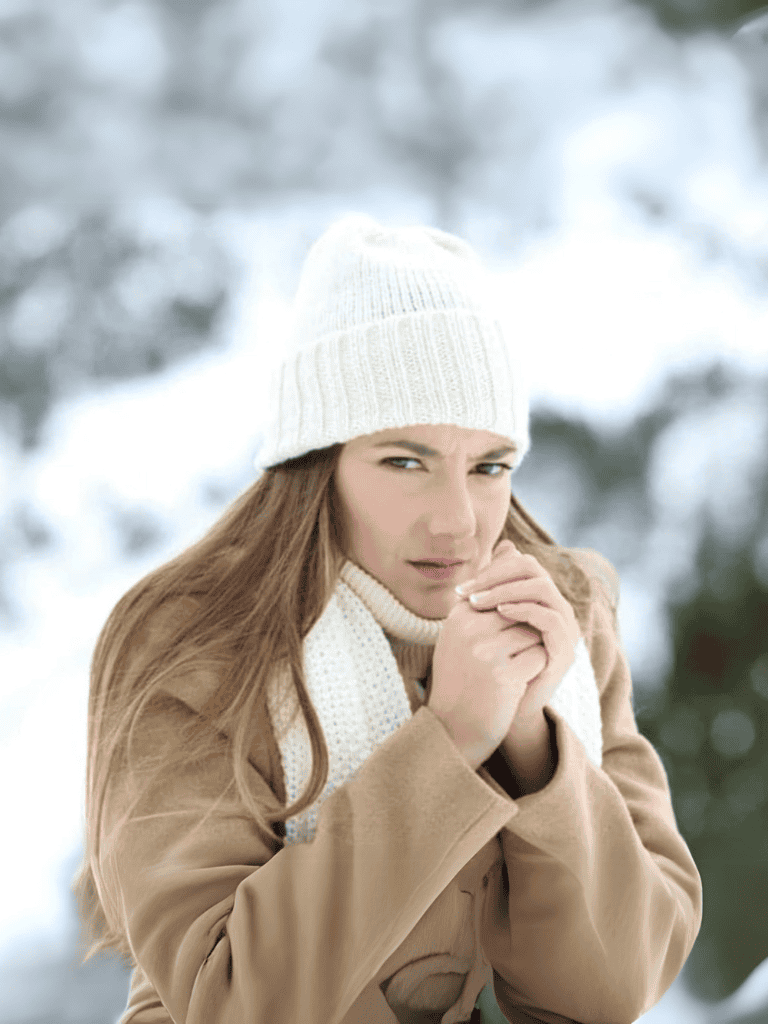 Woman bundled up in winter coat and white beanie, staying warm outdoors in cold weather.