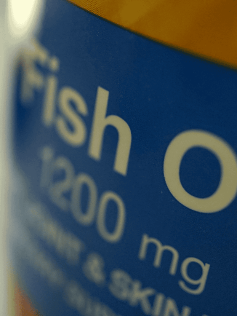 Close-up of blue fish oil supplement bottle label with text "Fish Oil 1200 mg" and "Omegas".