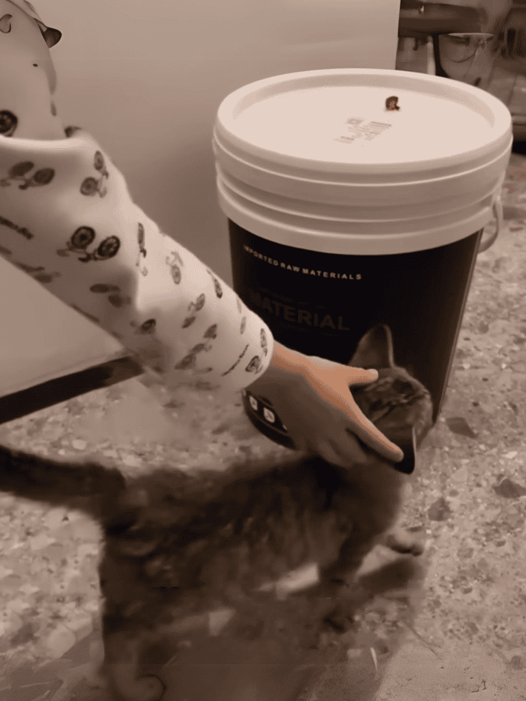 Small puppy eating from a container labeled "Material" on a granite surface.