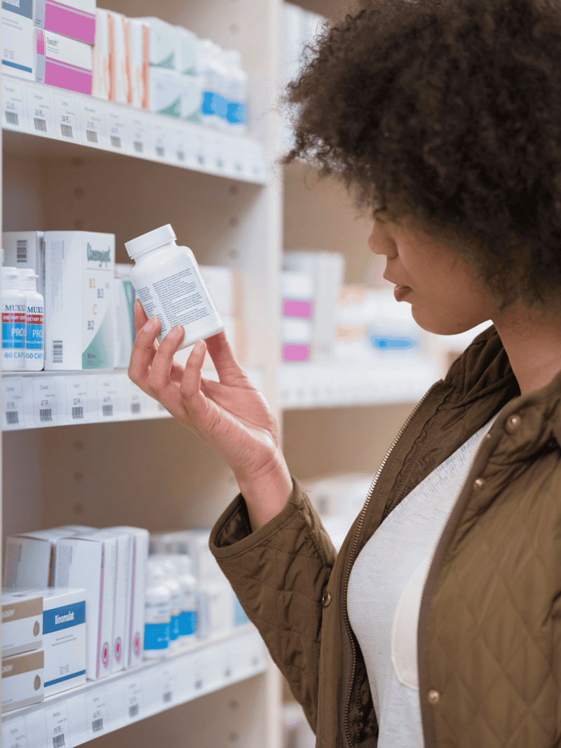 A woman selecting medication from a pharmacy shelf.