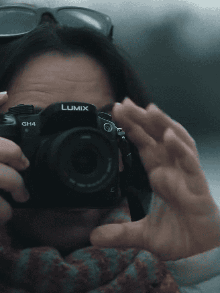 Woman taking a photo with a Lumix GH4 camera, close-up portrait, urban setting.