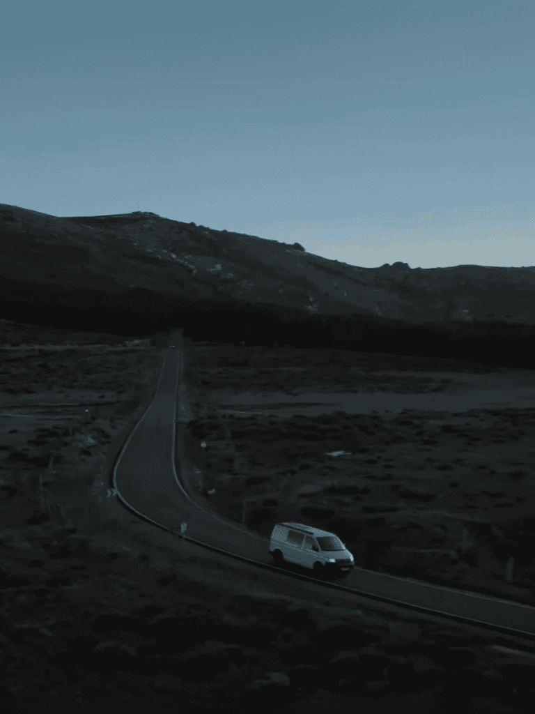 A white van driving along a winding mountain road at dusk.
