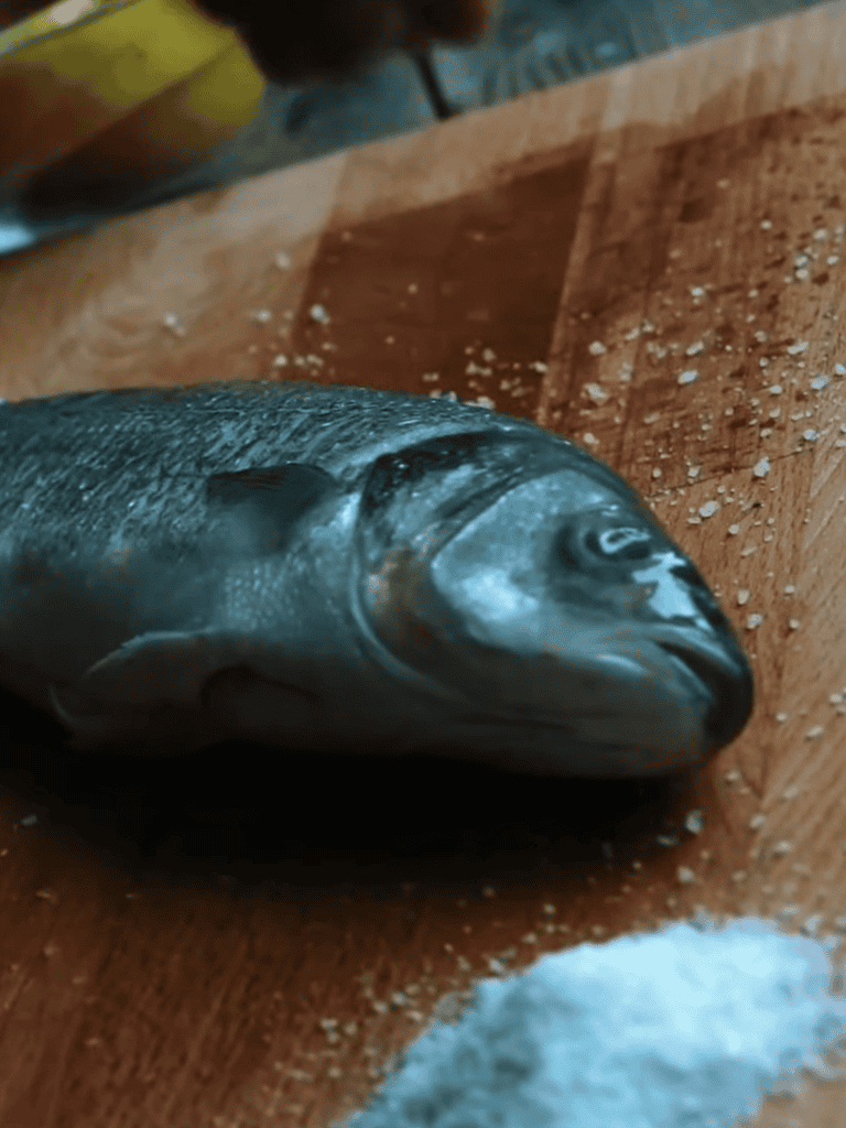Fresh fish prepared for cooking with salt on wooden surface.