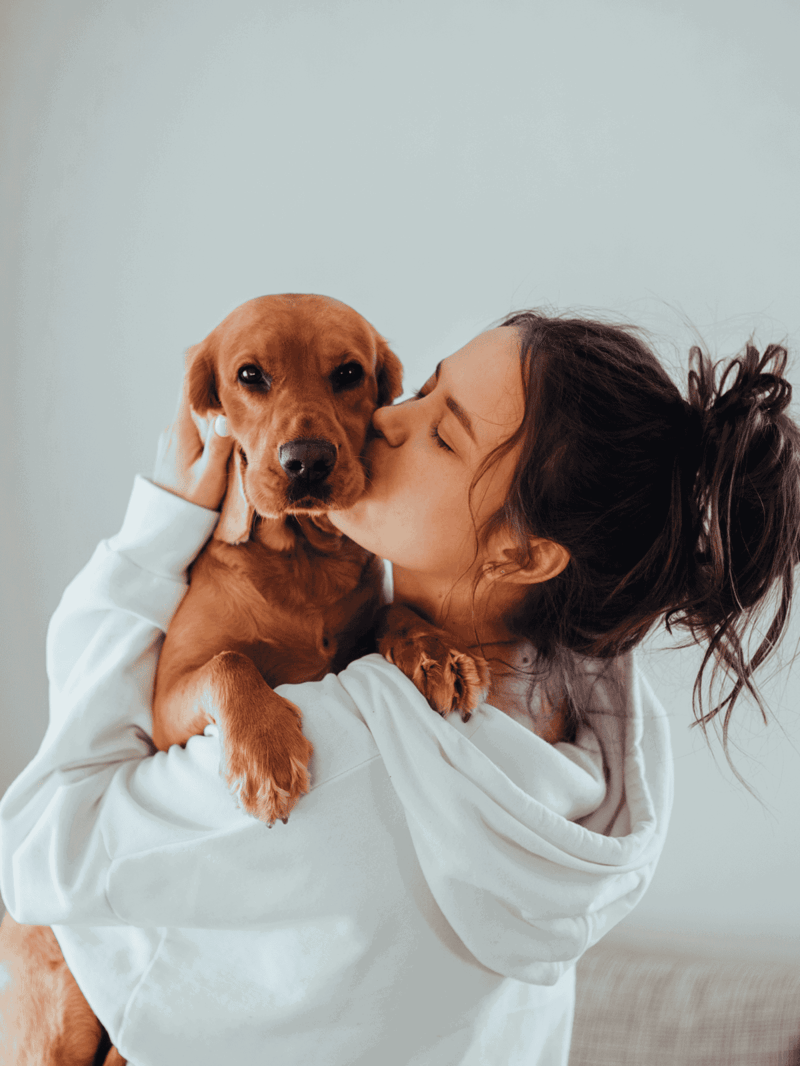 Happy woman kissing her cute puppy, emotional bond, pet companionship, dog care, cozy home setting.