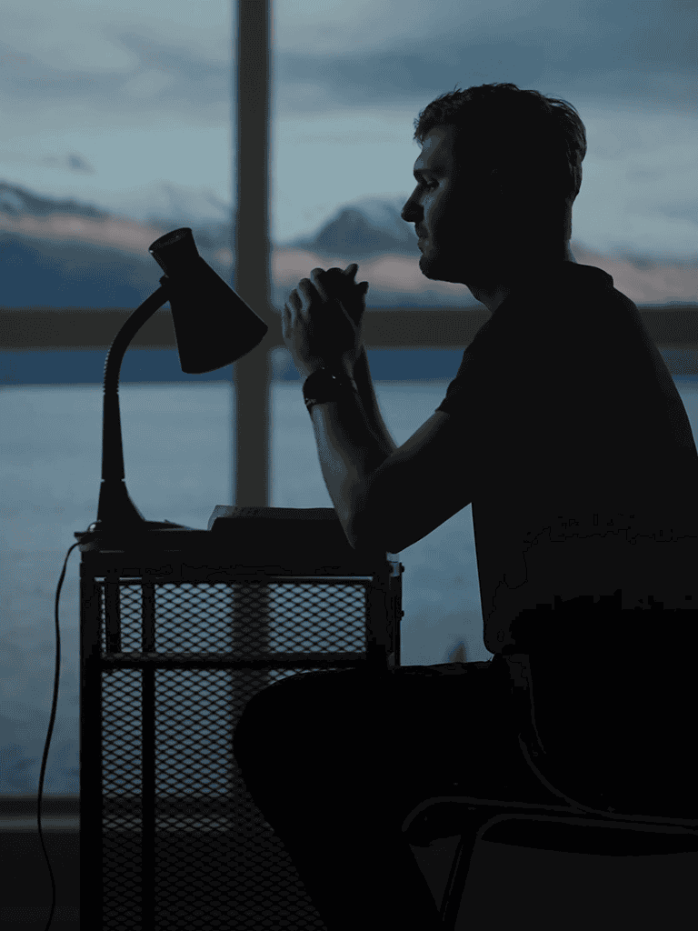 Silhouette of man sitting at desk by water, deep in thought with scenic backdrop.