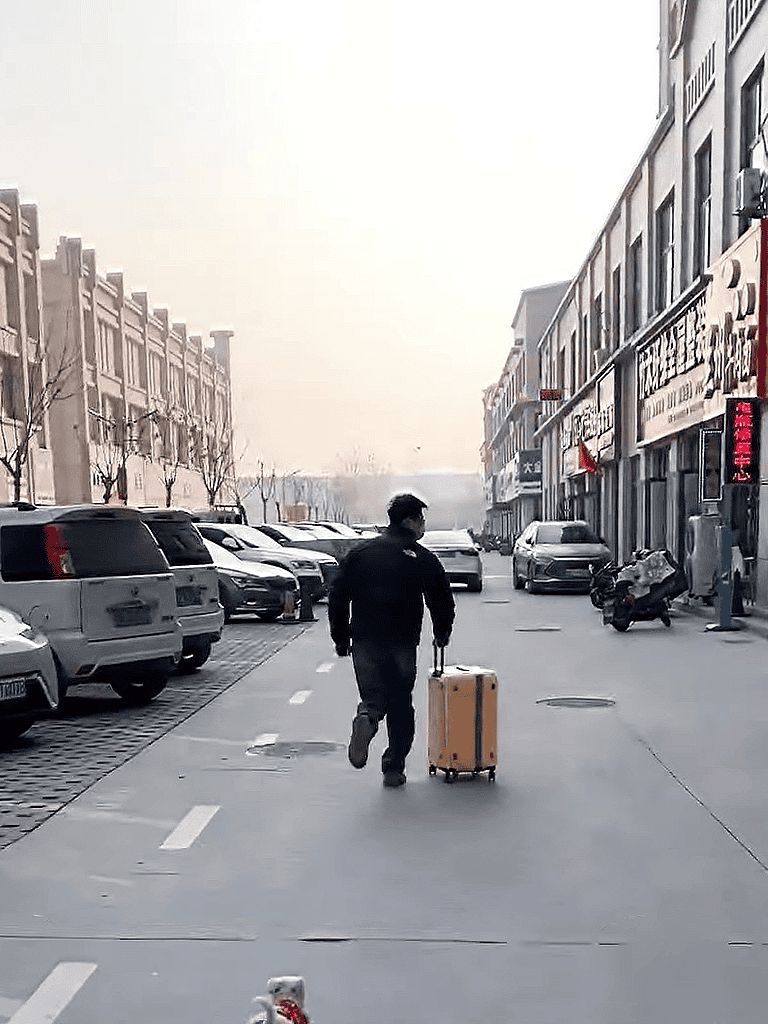 Person walking in city with rolling suitcase and pet carrier.